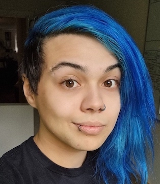 Portrait selfie of a 31 year old person with an olive skin tone. They have an undercut and medium legnth blue hair parted to the side. They are smiling and wearing a black shirt.